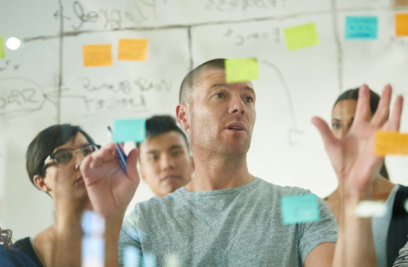 Team diskutiert Prozessschritte vor einer Glaswand mit Post-its – praktische Anwendung der Wertstromanalyse in der agilen Softwareentwicklung.